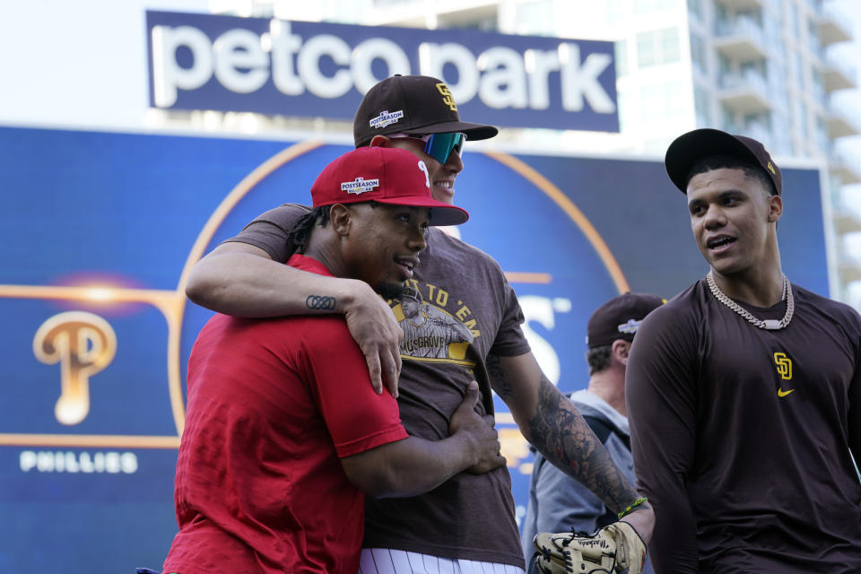 Philadelphia Phillies second baseman Jean Segura, left, hugs San Diego Padres third baseman Manny Machado as Padres right fielder Juan Soto, right, looks on during practice ahead of Game 1 of the baseball NL Championship Series Monday, Oct. 17, 2022, in San Diego. The Padres host the Phillies for Game 1 on Oct. 18. (AP Photo/Gregory Bull)