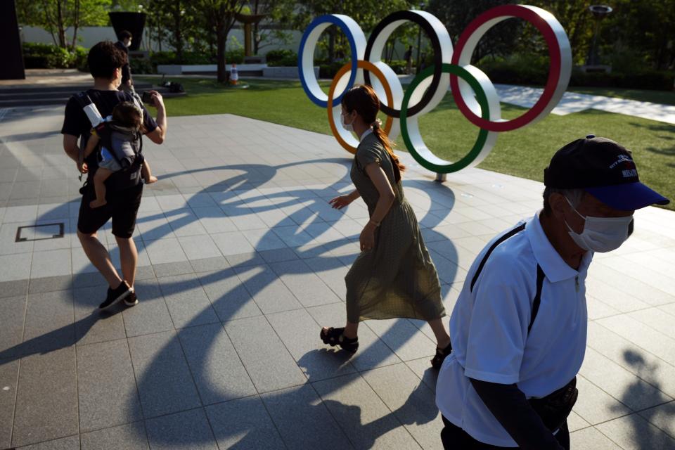People walking past the Olympic rings in Tokyo. The Japanese public has generally been opposed to the Games, partly over fears that coronavirus levels will spike as about 100,000 people enter the country (AP)