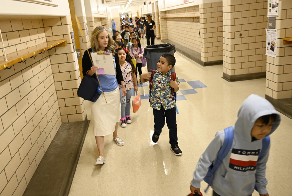 Elementary school students follow their teacher down a hallway to her classroom.