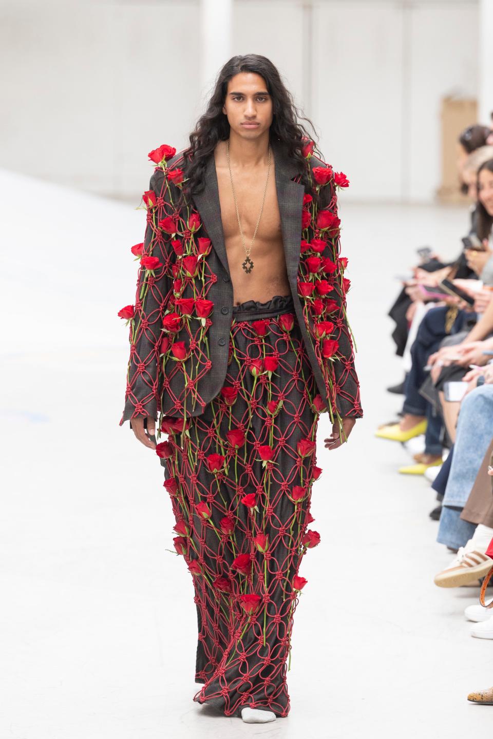 A runway model at the Rolf Ekroth show wearing a grey suit covered in fresh red stemmed roses