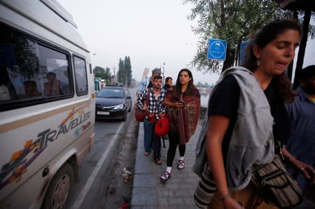 Foreign tourists carry their luggage as they walk on the banks of Dal Lake before leaving Srinagar