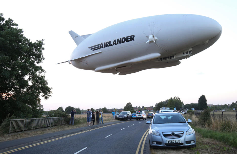 TOPSHOT - The Hybrid Air Vehicles HAV 304 Airlander 10 hybrid airship is seen in the air over a road on its maiden flight from Cardington Airfield near Bedford, north of London, on August 17, 2016. 
The Hybrid Air Vehicles 92-metre long, 43.5-metre wide Airlander 10, billed as the world's longest aircraft, lifted off for the first time from an airfield north of London. The Airlander 10 has a large helium-filled fabric hull and is propelled by four turbocharged diesel engines. According to the company it can stay airborne for up to five days at a time if manned, and for over 2 weeks unmanned with a cruising speed of just under 150 km per hour and a payload capacity of up to 10,000 kg. / AFP / JUSTIN TALLIS        (Photo credit should read JUSTIN TALLIS/AFP via Getty Images)