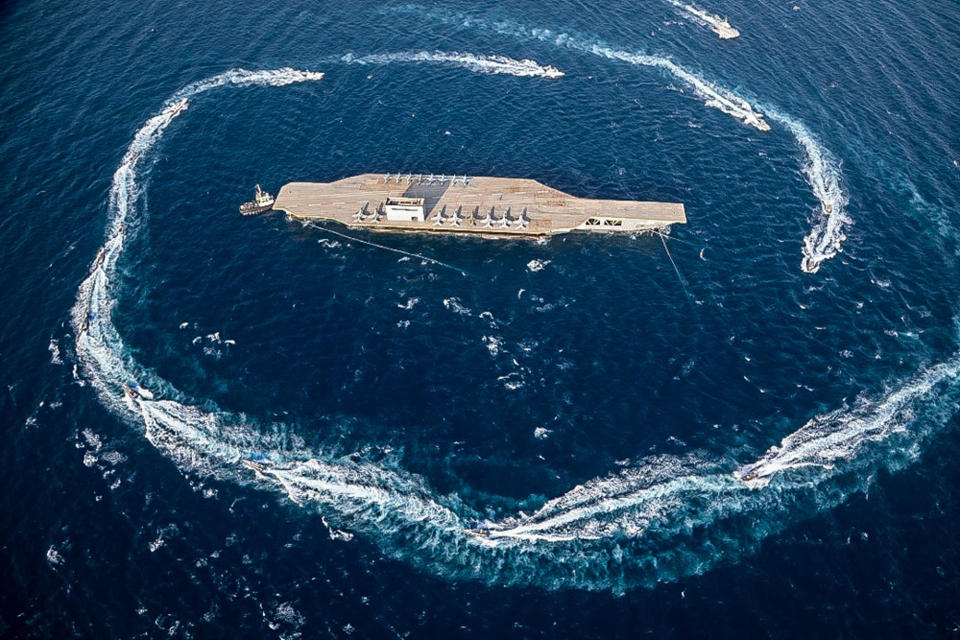 In this photo released Tuesday, July 28, 2020, by Sepahnews, Revolutionary Guard's speed boats circle around a replica aircraft carrier during a military exercise. Iran’s paramilitary Revolutionary Guard has fired a missile from a helicopter targeting the mock-up aircraft carrier in the strategic Strait of Hormuz. That's according to footage aired on state television on Tuesday. Iranian commandos also fast-roped down from a helicopter onto the replica in the footage from the exercise called “Great Prophet 14.” The drill appears aimed at threatening the U.S. amid tensions between Tehran and Washington. (Sepahnews via AP)