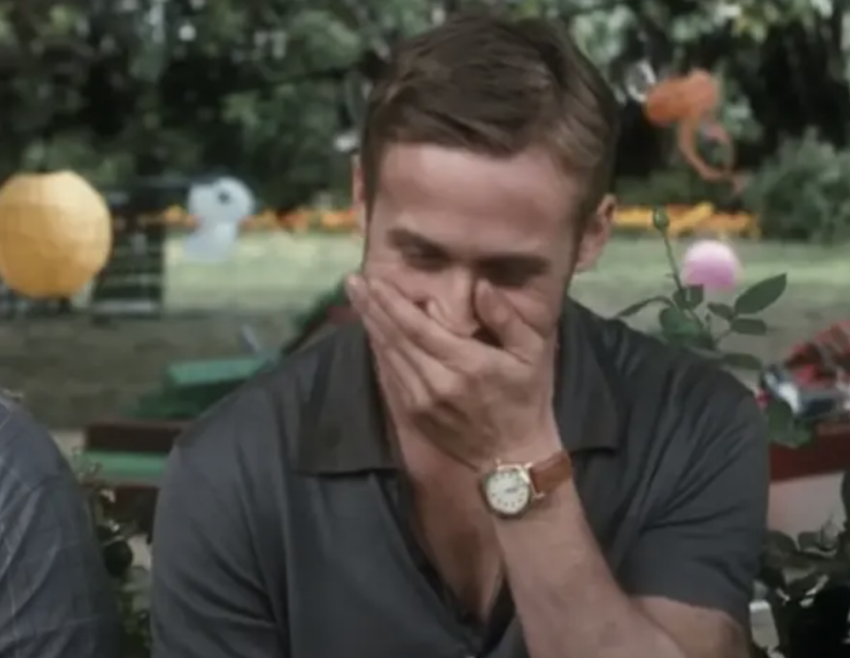 Ryan Gosling in a relaxed outdoor setting, laughing with his hand covering his mouth, wearing a casual short-sleeved shirt and a wristwatch