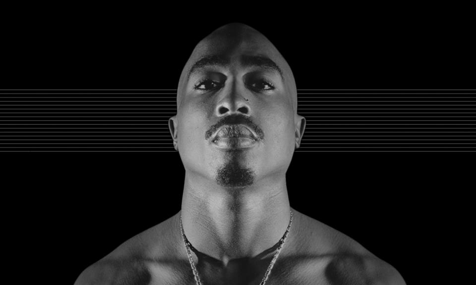 Photo of the late Tupac Shakur looking down at the camera against a black background with fine horizontal gray lines.