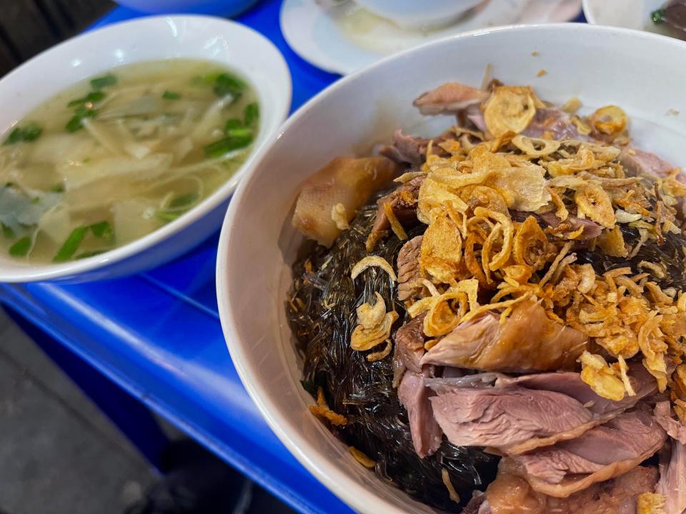 Bowl of glass noodles with goose and crunchy shallots on top.