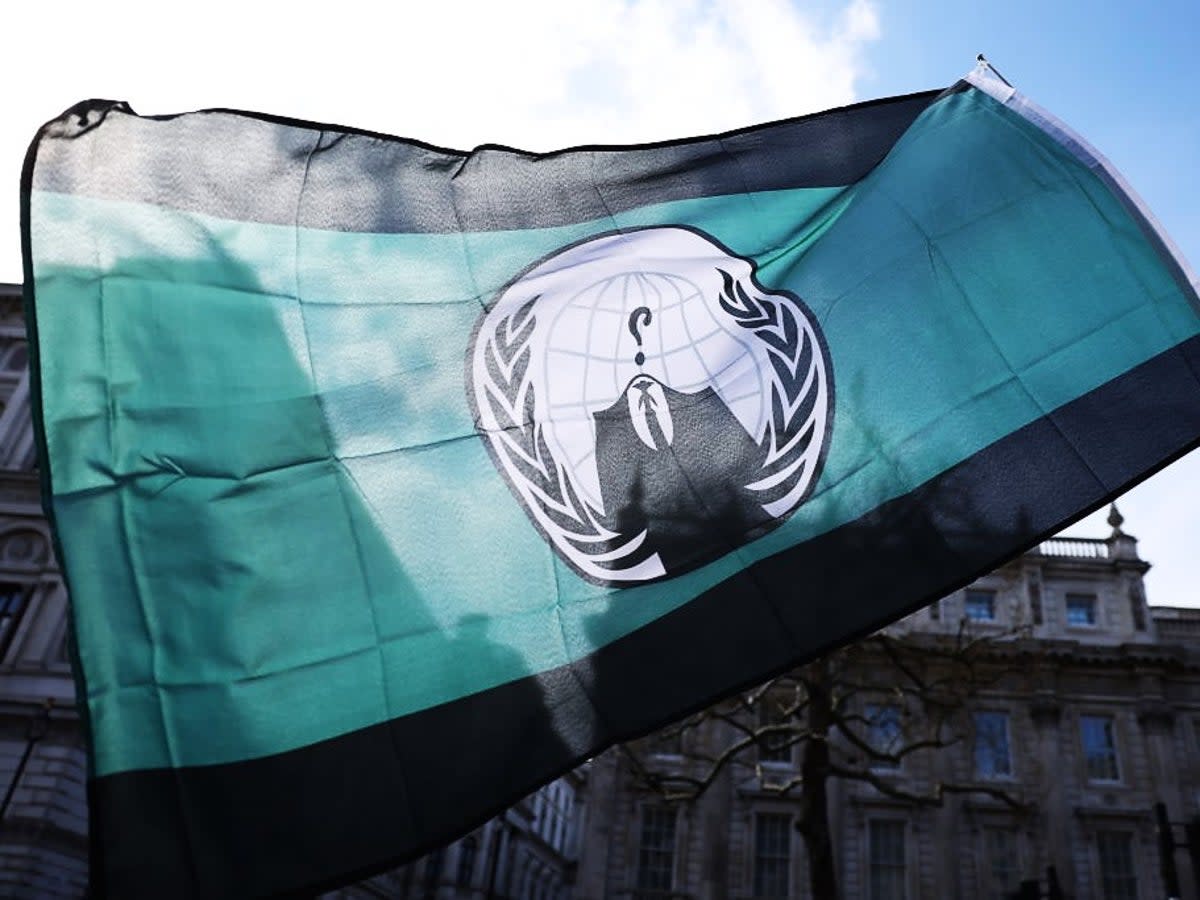 A demonstrator waves an ‘Anonymous’ hacking group flag during a protest in London on 2 April, 2022 (Getty Images)