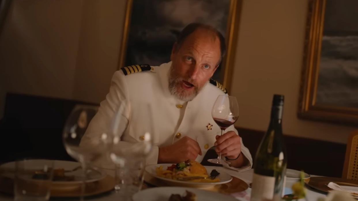  Woody Harrelson holding up a wine glass in Triangle of Sadness. 