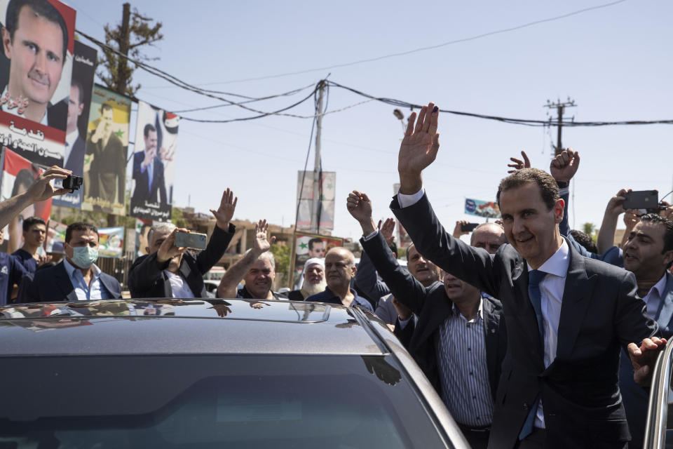 Syrian President Bashar Assad, right, waves for his supporters at a polling station during the Presidential elections in the town of Douma, in the eastern Ghouta region, near the Syrian capital Damascus, Syria, Wednesday, May 26, 2021. Syrians headed to polling stations early Wednesday to vote in the second presidential elections since the deadly conflict began in the Arab country. (AP Photo/Hassan Ammar)