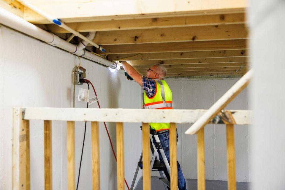 A worker in a yellow vest works on framing a basement. 