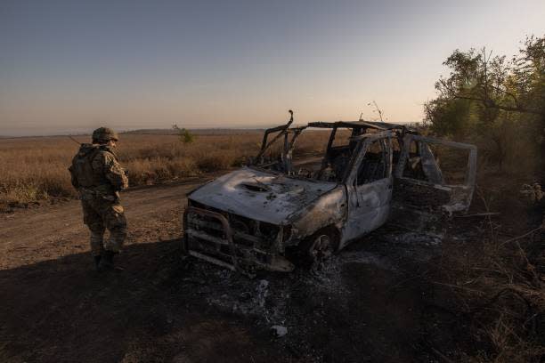 A Ukrainian soldier of the 65th Mechanized Brigade walks past a destroyed car, next to the trenches built by Russian forces, and that were captured by the Ukrainian army, near the frontline village of Robotyne, in the Zaporizhzhia region, on 1 October 2023 (AFP via Getty Images)