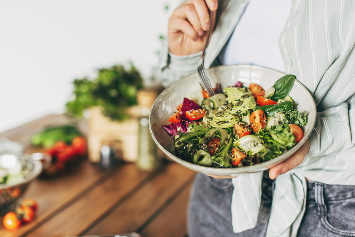 Woman mixing delicious superfood salad ingredients with wooden spoons in kitchen vegan