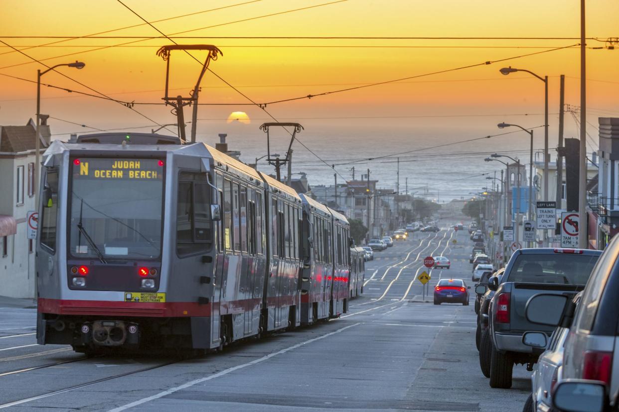 A group of light rail cars makes their way through San Francisco's Outer Sunset neighborhood. Pacific ocean on the background.