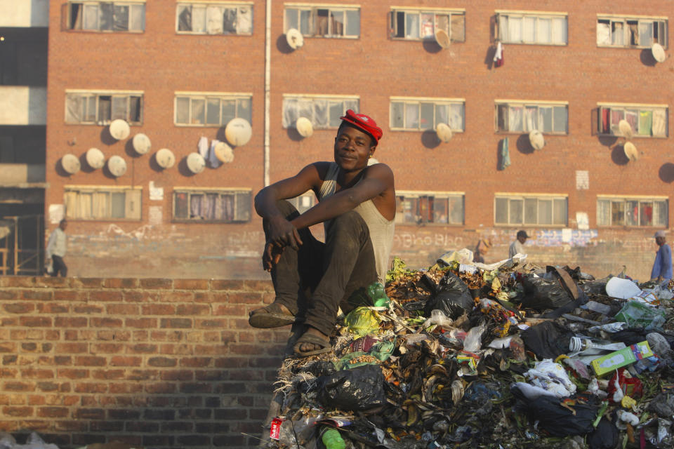 A man poses for a photo while seated on a dumpsite in Harare, Friday, 9, 2019. Fuel prices and the general cost of living continue to rise in Zimbabwe as the public struggle against basic shortages of water and power. (AP Photo/Tsvangirayi Mukwazhi)