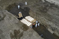 Workers wearing personal protective equipment bury bodies in a trench on Hart Island, Thursday, April 9, 2020, in the Bronx borough of New York. On Thursday, New York City’s medical examiner confirmed that the city has shortened the amount of time it will hold on to remains to 14 days from 30 days before they will be transferred for temporary internment at a City Cemetery. Earlier in the week, Mayor Bill DeBlasio said that officials have explored the possibility of temporary burials on Hart Island, a strip of land in Long Island Sound that has long served as the city’s potter’s field. (AP Photo/John Minchillo)