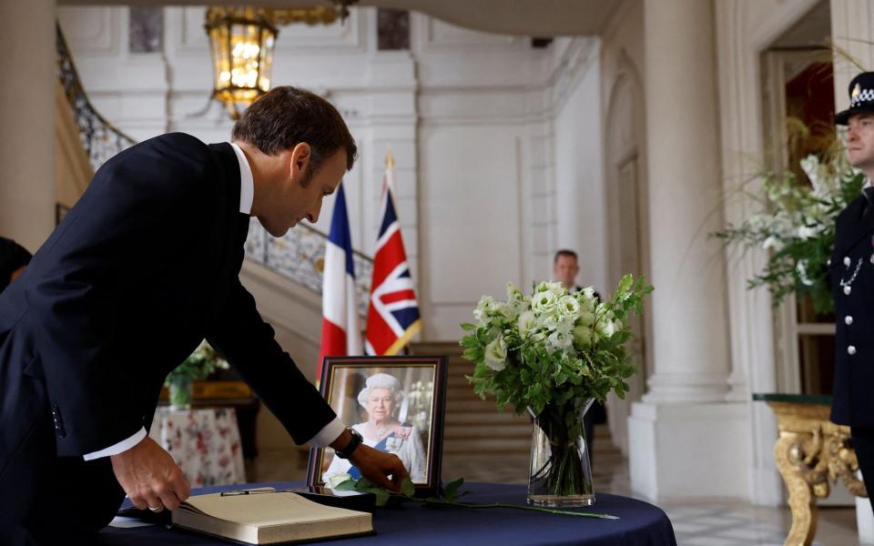 French President Emmanuel Macron places a white rose next to a portrait of Queen Elizabeth II during the signature of a condolence book - CHRISTIAN HARTMANN/POOL/EPA