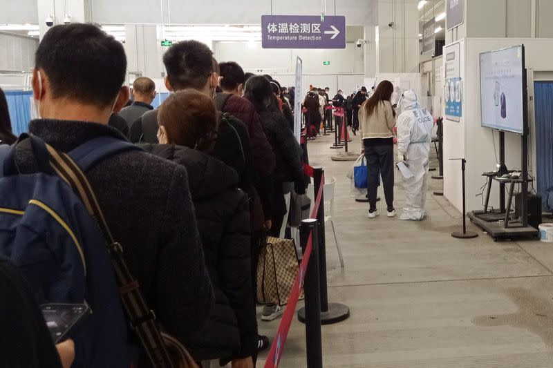 Passengers arriving on international flights wait in line next to a police officer wearing personal protective equipment (PPE) and speaking with a woman at the airport in Chengdu