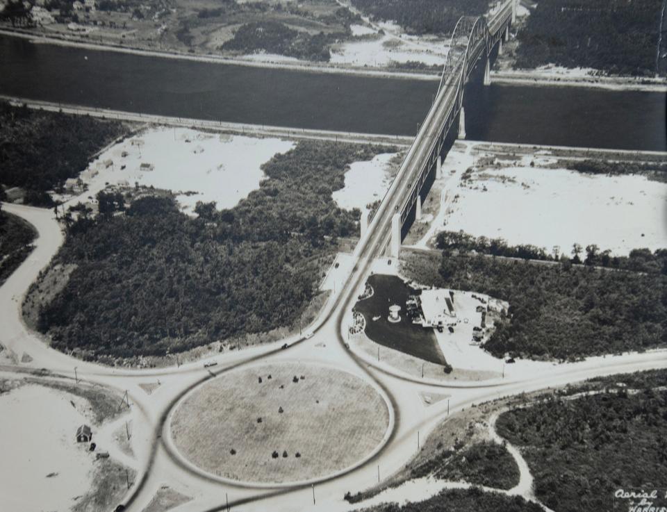 An aerial photo from the Bourne Historical Society's archives shows the Bourne Bridge and the small building at the bottom left, a tourist information booth. The photo dates to the 1930s and the old Howard Johnson's restaurant can be seen at right.