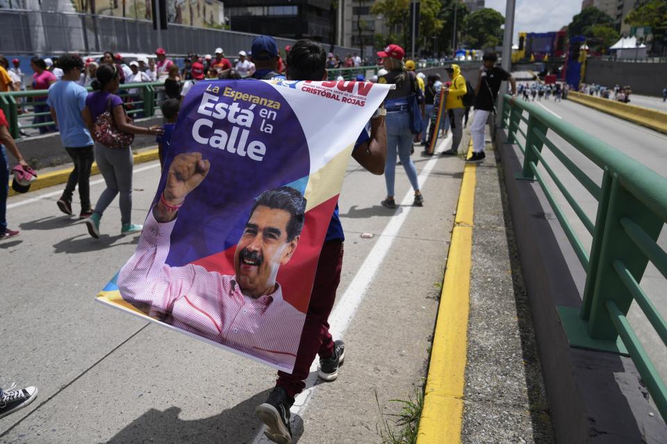 Un seguidor del presidente venezolano, Nicolás Maduro, con un cartel con su imagen camino a un acto por el inicio oficial de la campaña para las elecciones presidenciales del 28 de julio en Caracas, Venezuela, el jueves 4 de julio de 2024. (AP Foto/Ariana Cubillos)