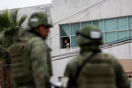 A woman holds her dog while looking out of a window at soldiers next to the Colegio Americano del Noreste after a student opened fire at the American school in Monterrey, Mexico January 18, 2017. REUTERS/Daniel Becerril