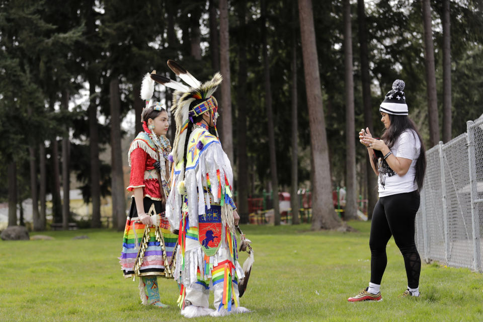 In this photo taken Saturday, April 4, 2020, Wicahpi Cuny, left, and her brother Wakiyan Cuny, Dakota and Lakota tribal members, are filmed by their mother Tera Baker during a live streamed powwow from a park near their home in Puyallup, Wash. The largest powwows in the country have been canceled or postponed amid the spread of the coronavirus. Tribal members have found a new outlet online with the Social Distance Powwow. They're sharing videos of colorful displays of culture and tradition that are at their essence meant to uplift people during difficult times. (AP Photo/Elaine Thompson)