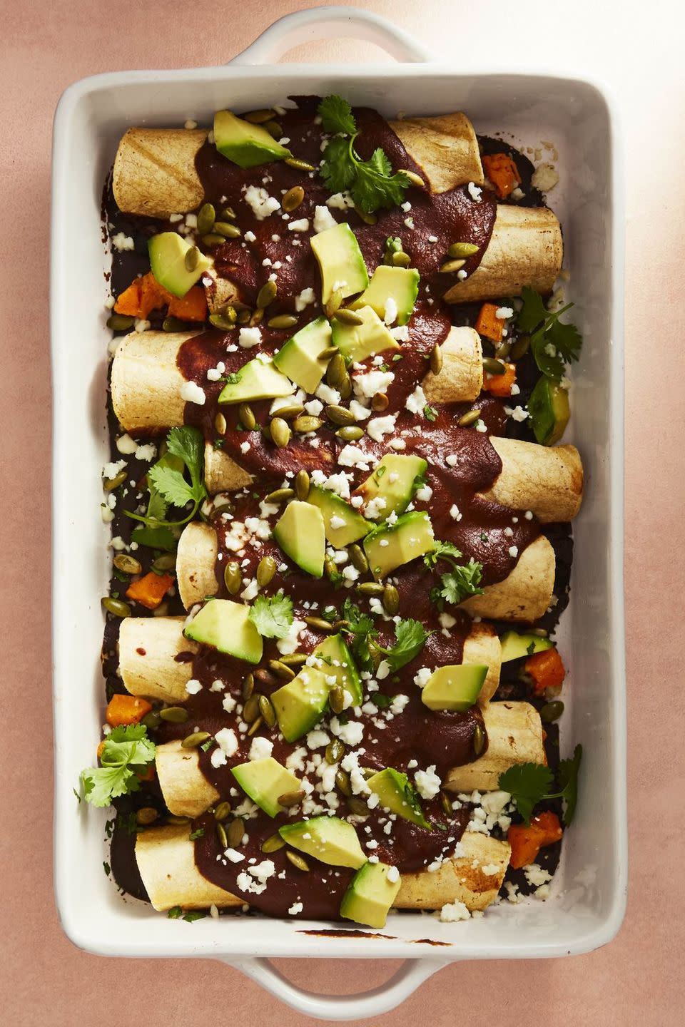 butternut squash mole enchiladas with avocado on top in a white baking dish