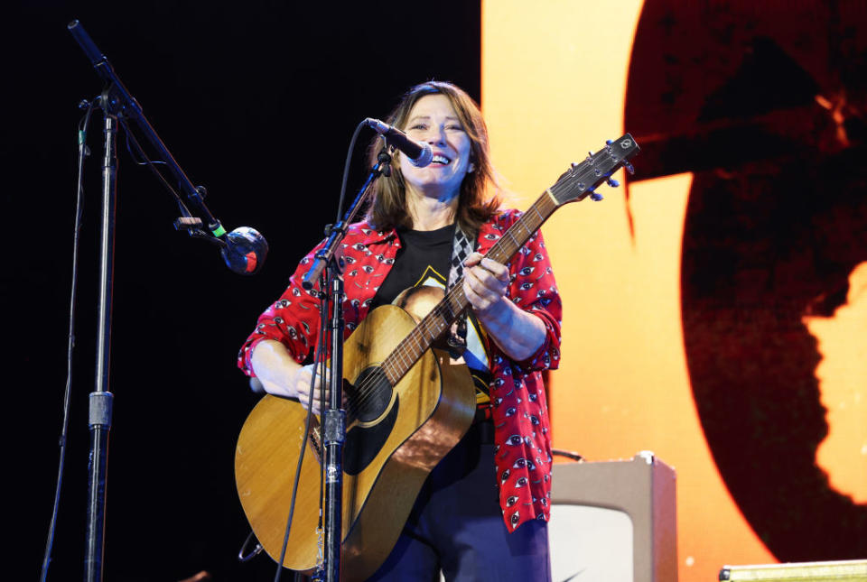 Kim on stage performing with a guitar during a concert, wearing a patterned shirt and pants