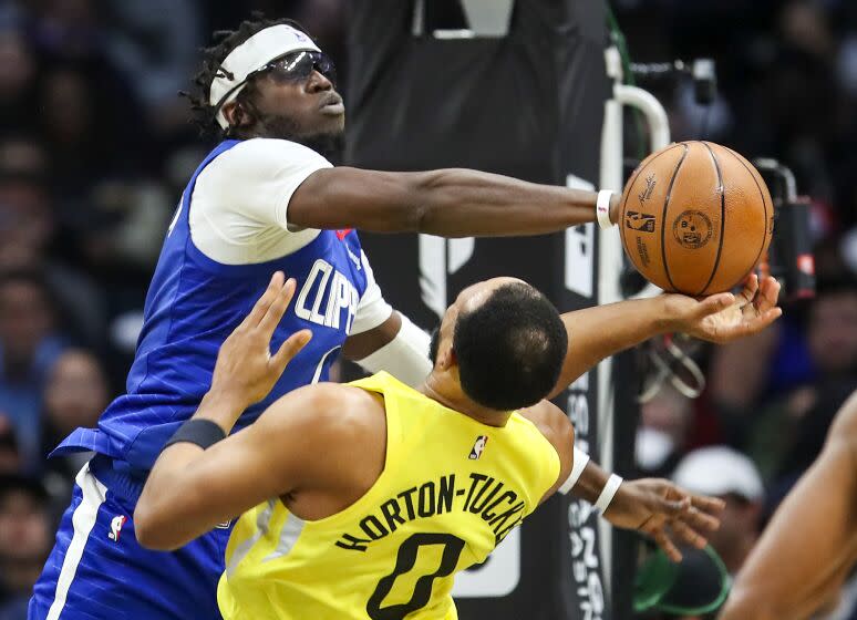 Clippers guard Reggie Jackson, #1, left, fouls Utah guard Talen Horton-Tucker as he goes up for a shot.