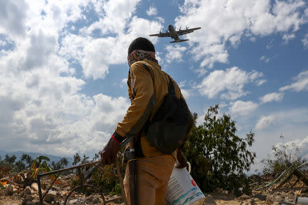 A villager carries his belongings as a military aircraft is about to land in an area after an earthquake hit Petobo neighbourhood in Palu, Indonesia, October 6, 2018. REUTERS/Athit Perawongmetha