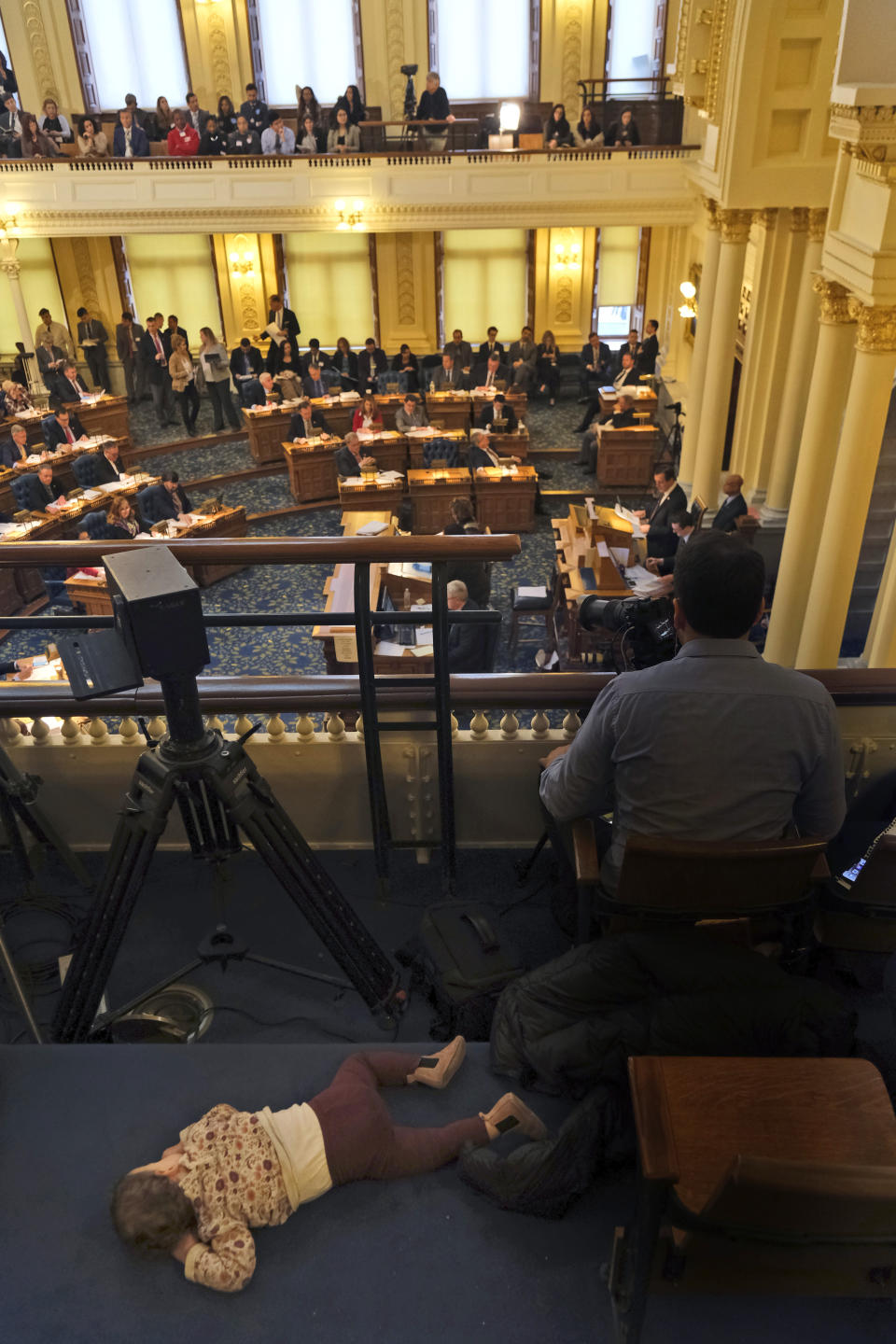 A child sleeps on the floor of the balcony while the assembly conducts business at the state house in Trenton, N.J., Monday, Jan. 13, 2020. The prospects of a vote on legislation to eliminate most religious exemptions for vaccines for schoolchildren in New Jersey looked uncertain Monday, according to the bill's sponsor, as opponents crowded the Statehouse grounds with flags, bullhorns and banners. (AP Photo/Seth Wenig)