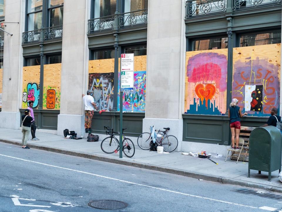 Artists paint on the boarded-up windows of Alo Yoga in SoHo on June 20, 2020 in New York City.