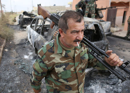 A Kurdish Peshmerga fighter walks in front of destroyed vehicles belonging to Islamic State militants in Tel Asqof, northern Iraq May 4, 2016. REUTERS/Goran Tomasevic