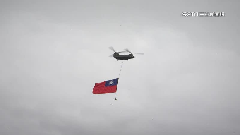 直升機吊掛著巨幅國旗飛越總統府上空，一邊播放著國歌鼓舞士氣。