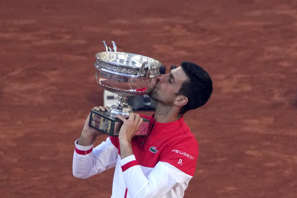 FILE- In this June 13, 2021, file photo, Serbia's Novak Djokovic kisses the trophy after defeating Stefanos Tsitsipas, of Greece, 6-7 (6), 2-6, 6-3, 6-2, 6-4 in the final of the French Open tennis tournament at the Roland Garros stadium in Paris. Djokovic is 26-0 in Grand Slam matches in 2021, moving him two victories away from being the first man to win all four major tennis championships in one season since Rod Laver in 1969. (AP Photo/Christophe Ena, File)