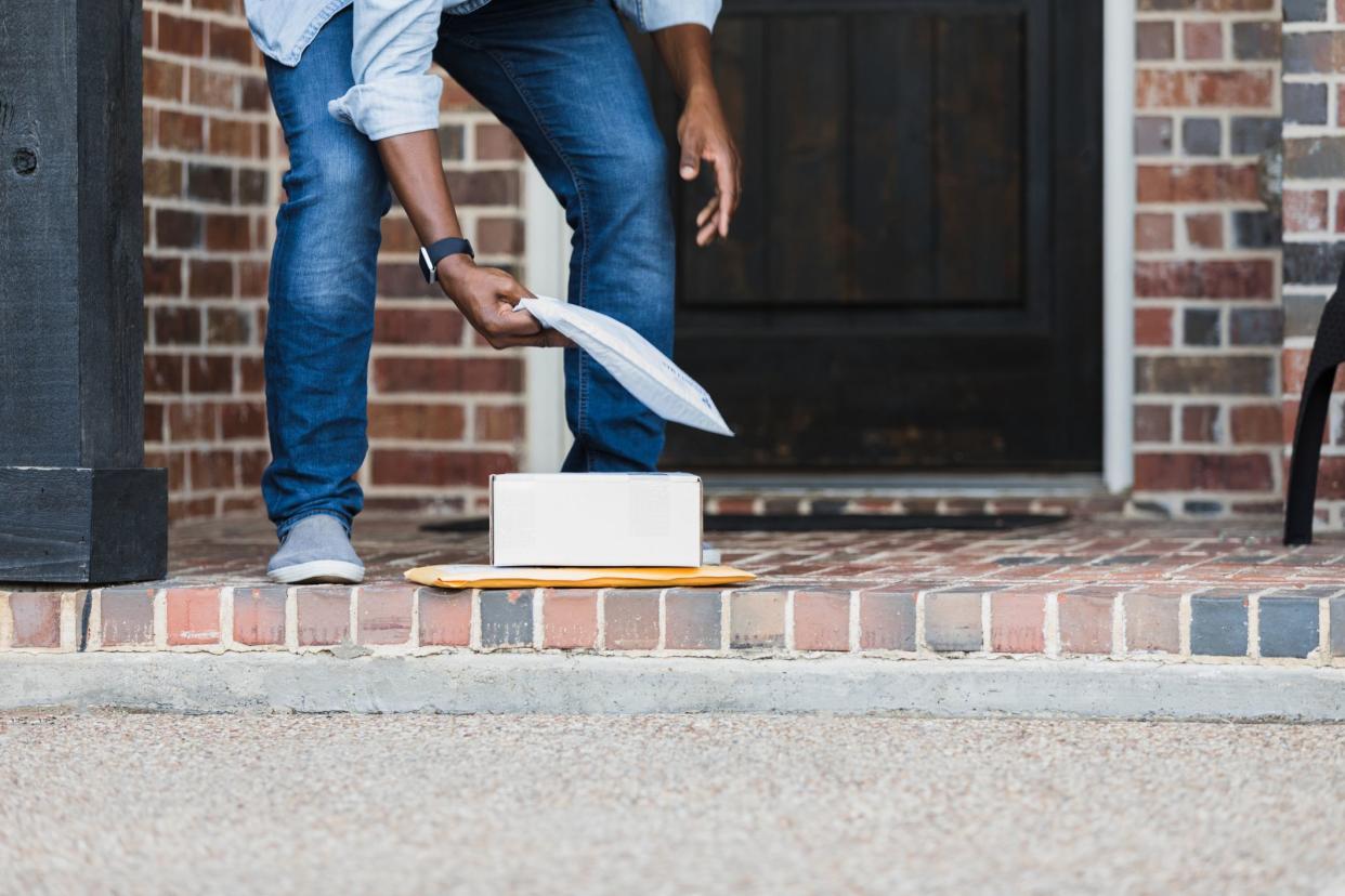 An unrecognizable man bends over to pick up packages that were left on his front porch by a delivery driver.