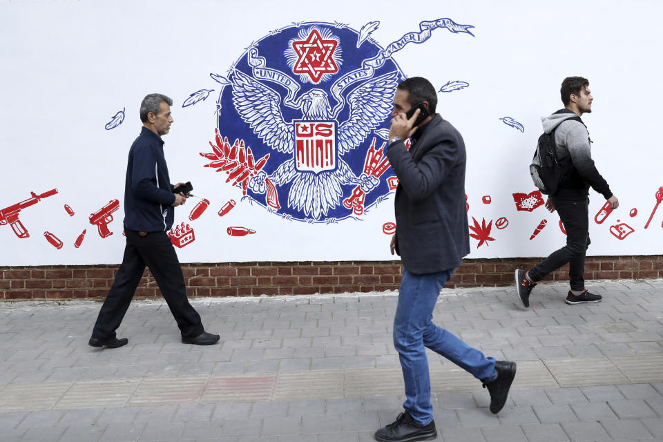People walk past a satirical drawing of the Great Seal of the United States after new anti-U.S. murals on the walls of former U.S. embassy unveiled in a ceremony in Tehran, Iran, Saturday, Nov. 2, 2019. Anti-U.S. works of graphics is the main theme of the wall murals painted by a team of artists ahead of the 40th anniversary of the takeover of the U.S. diplomatic post by revolutionary students. (AP Photo/Vahid Salemi)