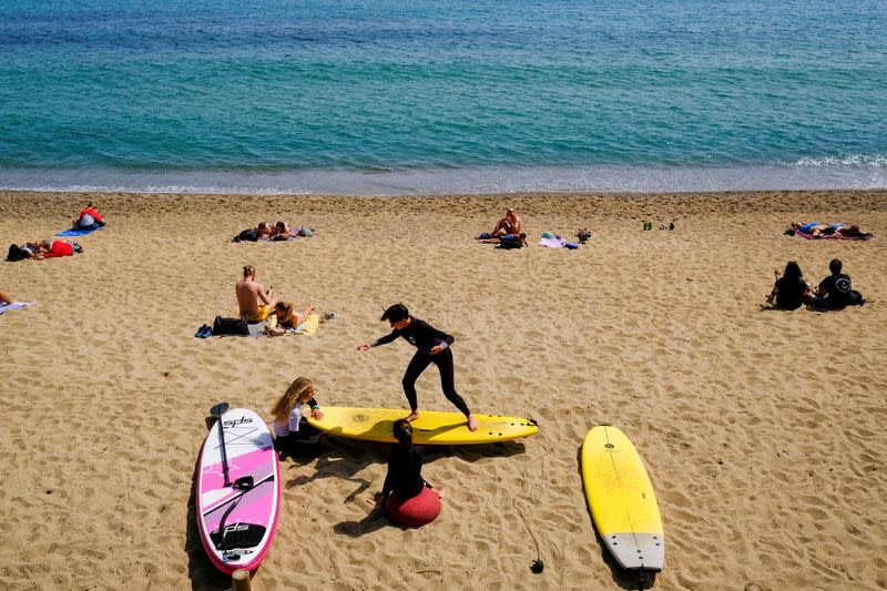 FILE PHOTO: A person teaches surfing to children at Barceloneta beach, in Barcelona