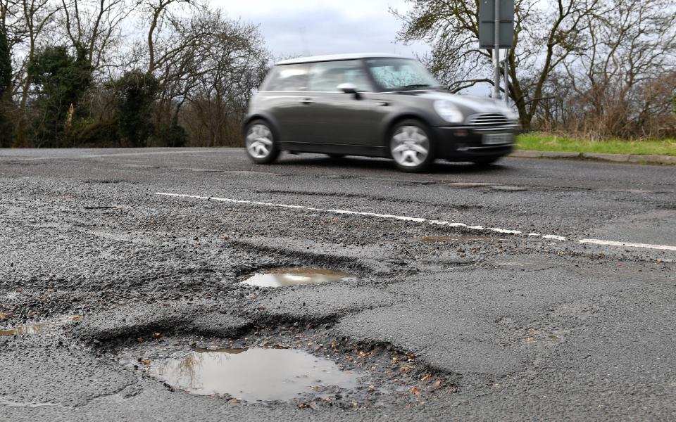 A car passing potholes in a road near Peterborough in Cambridgeshire.