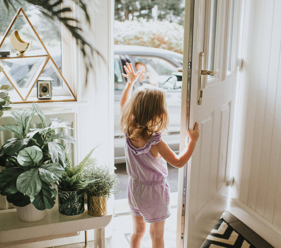 Cute little girl waving out the door in a sunny hallway.