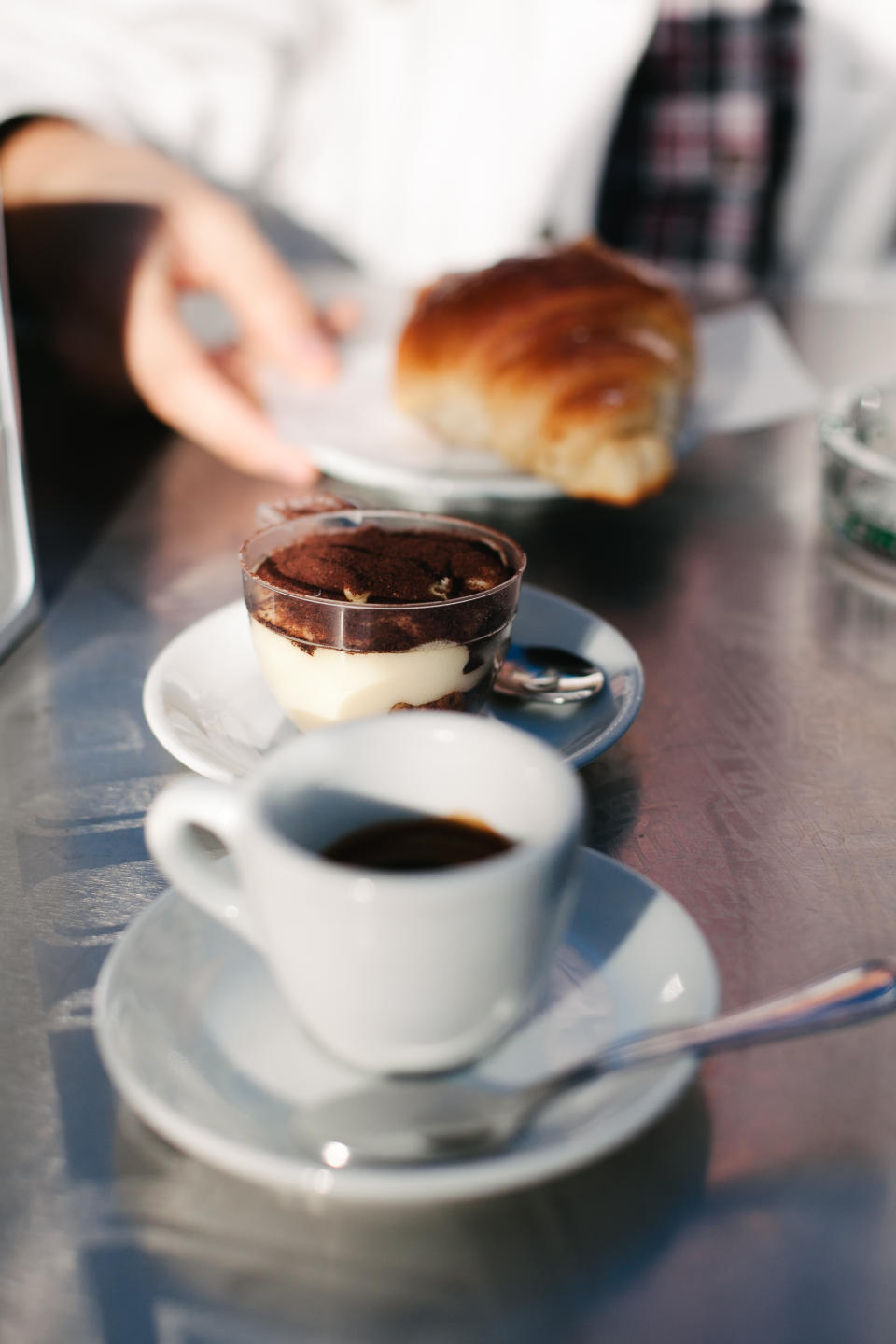 Two cups of coffee on a table with a partially eaten croissant. A person's hands are in view