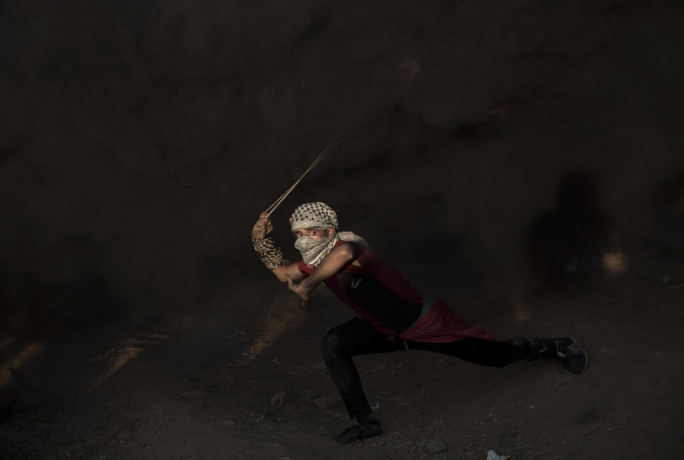 A Palestinian protester hurls stones towards Israeli troops during a protest at the Gaza Strip's border with Israel, Friday, Oct. 12, 2018. (AP Photo/Khalil Hamra)