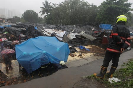A fireman looks on as rescue workers search for survivors under the cover of a tarpaulin after a wall collapased on hutments due to heavy rains in Mumbai