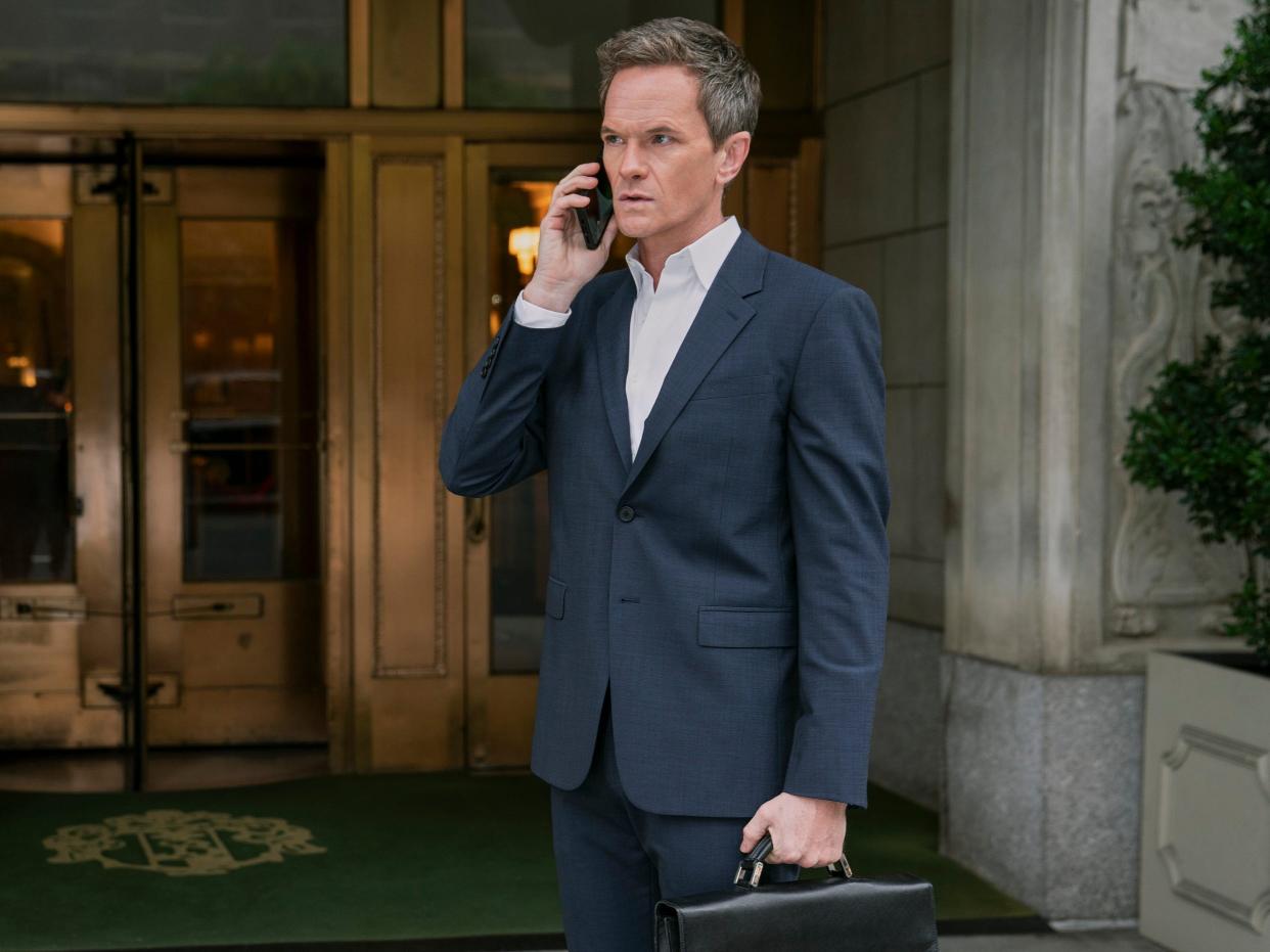 Neil Patrick Harris standing on the phone with a blue suit and briefcase