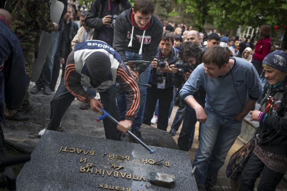 Pro-Russian protesters break up the words "Ukrainian the Security Service" next to the Ukrainian regional office of the Security Service in Donetsk, eastern Ukraine, Saturday, May 3, 2014, which has been captured to honor the memory of fallen comrades during fighting with pro-Ukrainian activists in Odessa on Friday. In Donetsk, the largest city in the insurgent east, demonstrators who stormed the local office of the Ukrainian Security Service on Saturday evening shouted "We will not forgive Odessa." No police were deployed to block the building takeover. (AP Photo/Alexander Zemlianichenko)