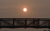 A person crosses a bridge against a hazy sunset over Century Park in Vernon Hills, Ill,, Tuesday, Sept. 15, 2020. The smoke from dozens of wildfires in the western United States has now blanket much of the county along with parts of Mexico and Canada, as residents thousands of miles away on the East Coast are being treated to unusually hazy skies and remarkable sunsets. (John Starks/Daily Herald via AP)