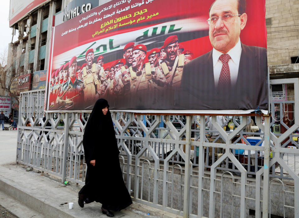 In this Tuesday, March 18, 2014 photo, an Iraqi woman walks past an anti-terrorism banner with a photo of Iraqi Prime Minister Nouri al-Maliki, in Baghdad, Iraq. Islamic militants who took over the Iraqi city of Fallujah are now trying to show they can run it, providing social services, policing the streets and implementing Shariah rulings in a bid to win the support of its Sunni Muslim population. Partial translation of Arabic on banner reads, "the media supports security forces efforts to capture terrorists and resume safety." (AP Photo/Karim Kadim)