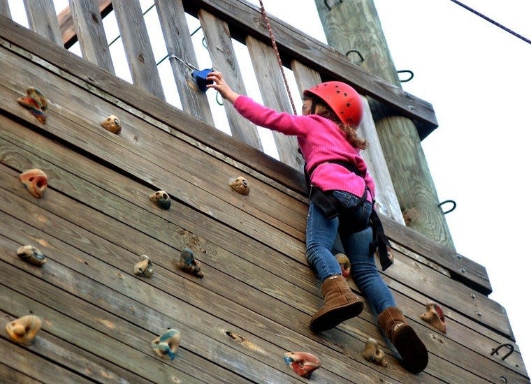 A young camper reaches a bell atop a rock-climbing wall in this file photo from Camp Ockanickon.