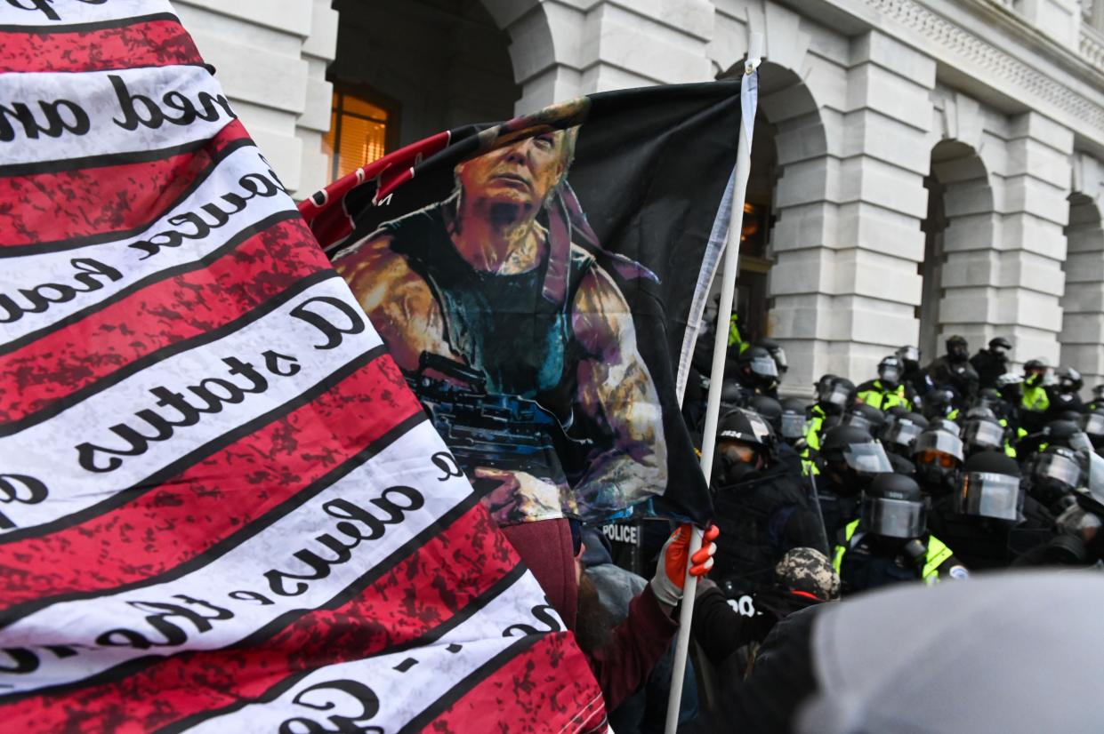 People hold flags as riot police push back a crowd of supporters of then-President Donald Trump after they stormed the Capitol building on January 6, 2021 in Washington, DC.