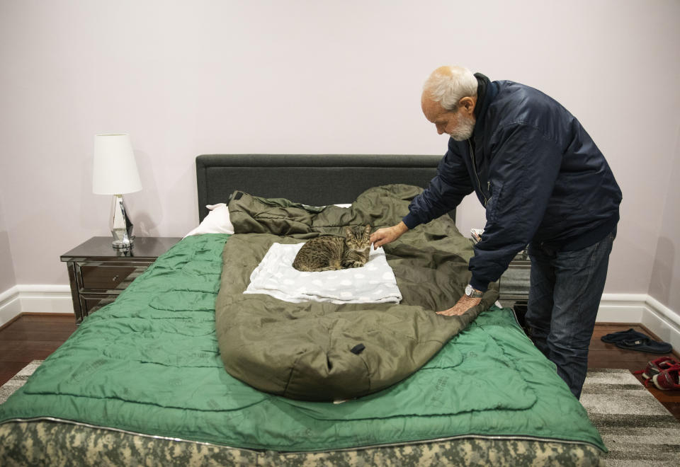 David Tonkin pets Ned, his son Matthew's cat, that now sleeps on David's bed on the sleeping bag Matthew used in Afghanistan, in Perth, Australia, Sunday, July 21, 2019. After Matthew died, and for years to come, David would suddenly awaken at 10 p.m. _ the same time that Matthew used to call from Afghanistan. Now, instead of Matthew's voice, there is only silence. Just like the silence from the officials he believes did little to prevent the death of his son. (AP Photo/David Goldman)