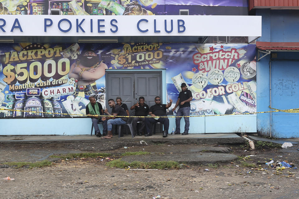 Locals gather outside closed shops in Honiara, Solomon Islands, Monday, Dec. 6, 2021. Lawmakers in the Solomon Islands are debating whether they still have confidence in the prime minister, after rioters last month set fire to buildings and looted stores in the capital.(Gary Ramage via AP)